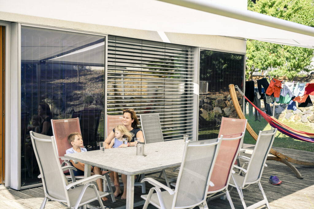 Junge Frau sitzt mit zwei Kindern auf der Terrasse ihre Einfamilienhauses.