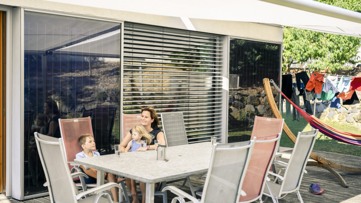 Junge Frau sitzt mit zwei Kindern auf der Terrasse ihre Einfamilienhauses.